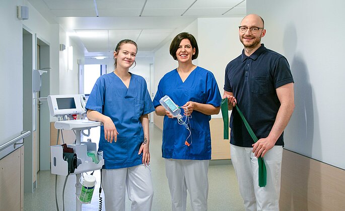 Zwei Mitarbeiterinnen aus der Pflege und ein Mitarbeiter der physikalischen Therapie stehen in einem Gang des Klinikums Wetzlar
