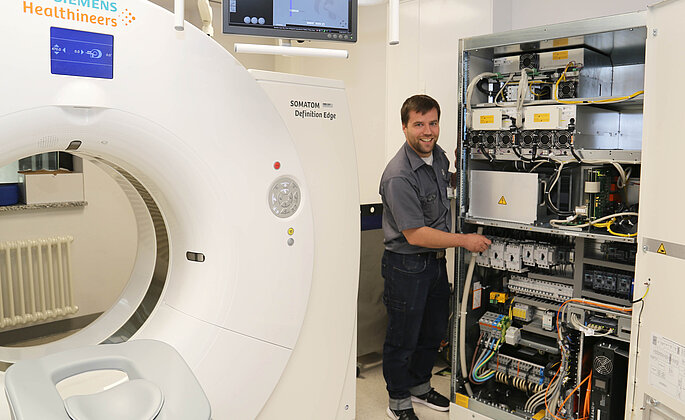Mitarbeiter der Medizintechnik arbeitet an einem Schaltschrank eines CTs. 