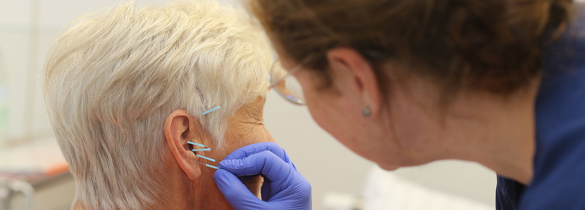 Mitarbeiterin setzt Akupunkturnadeln am Ohr einer Patientin. 