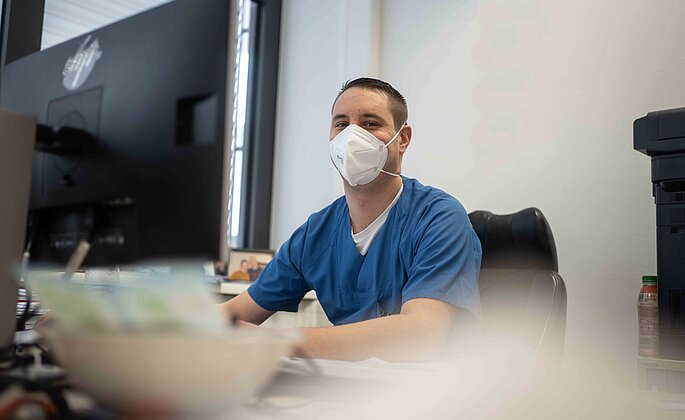Pflegerischer Leiter der Notaufnahme sitzt an seinem Arbeitsplatz vor einem Bildschirm und schaut in die Kamera. Georg Pfaff, Klinikum Wetzlar. 
